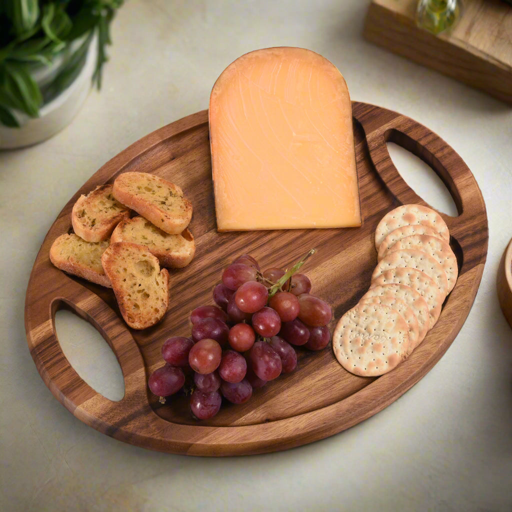 Wooden cutting board with cheese, crackers, and grapes on a light surface.