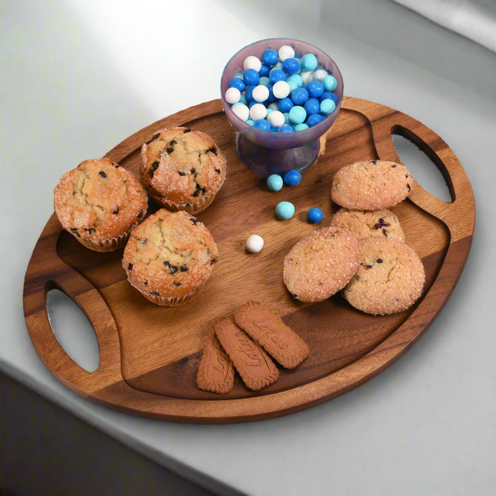 Wooden tray with muffins, cookies, and blue and white candies on a light gray surface.