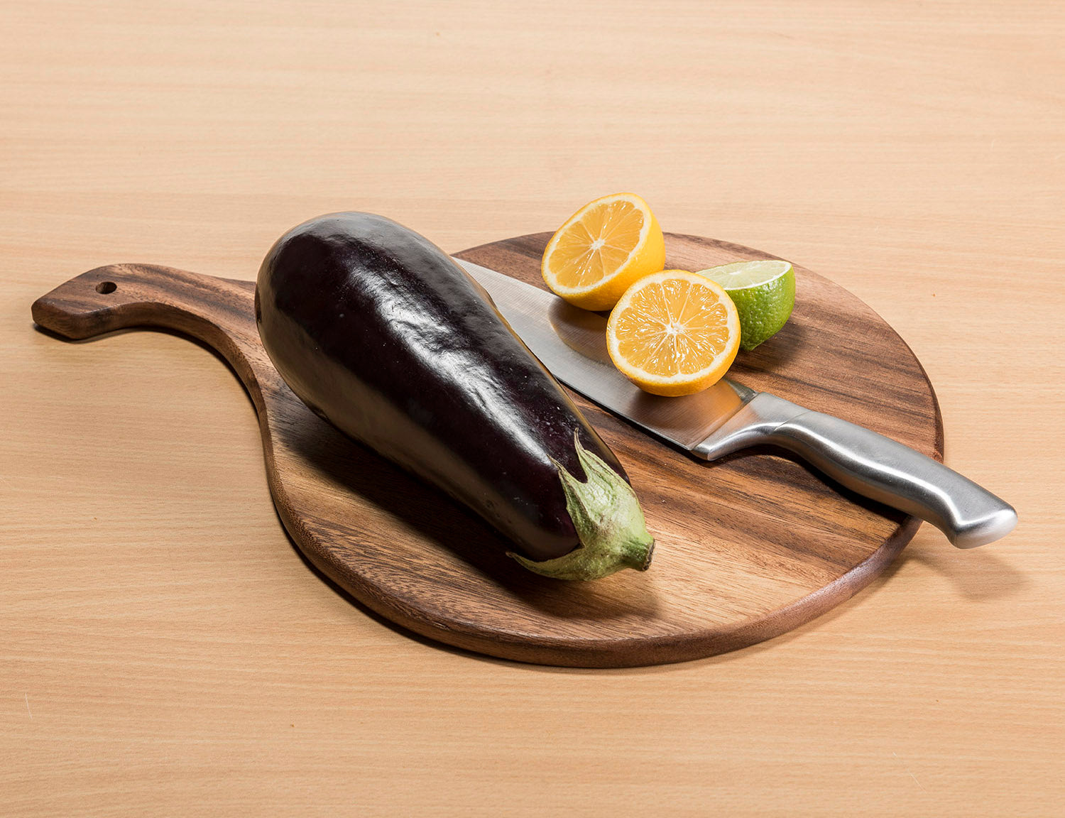 Eggplant, lemon, and lime on a wooden cutting board with a knife.