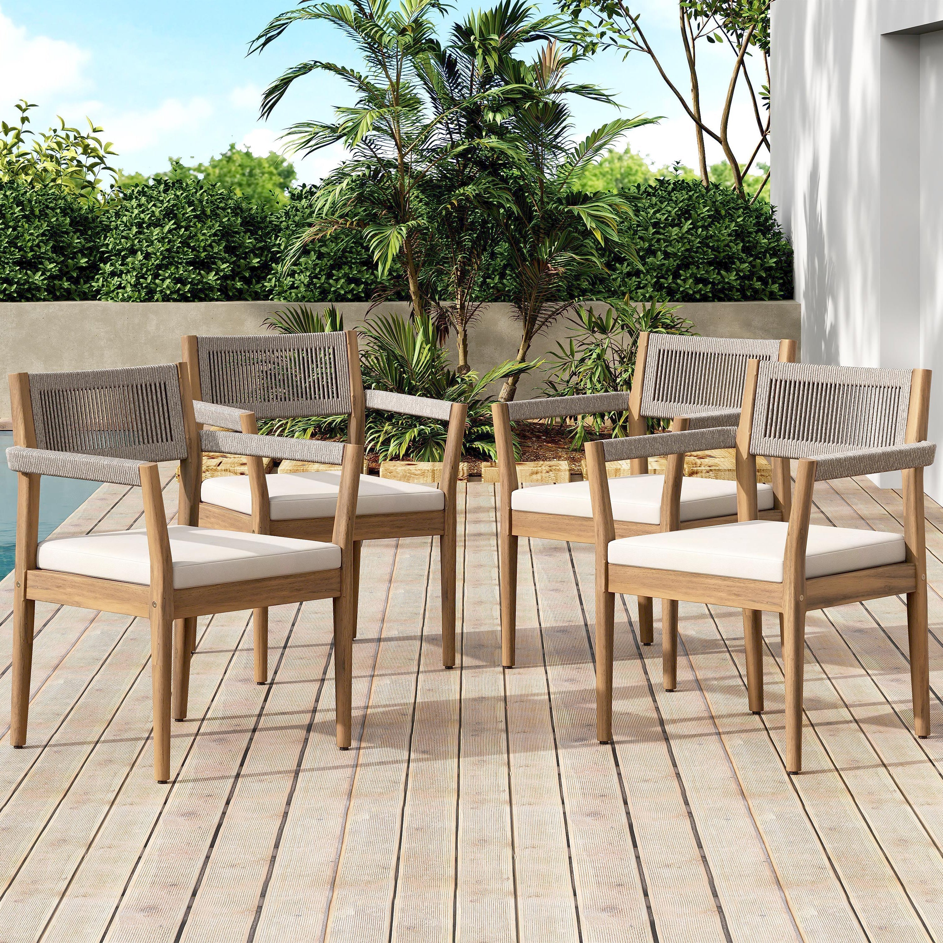 Set of four wooden outdoor chairs with white cushions on a wooden deck.