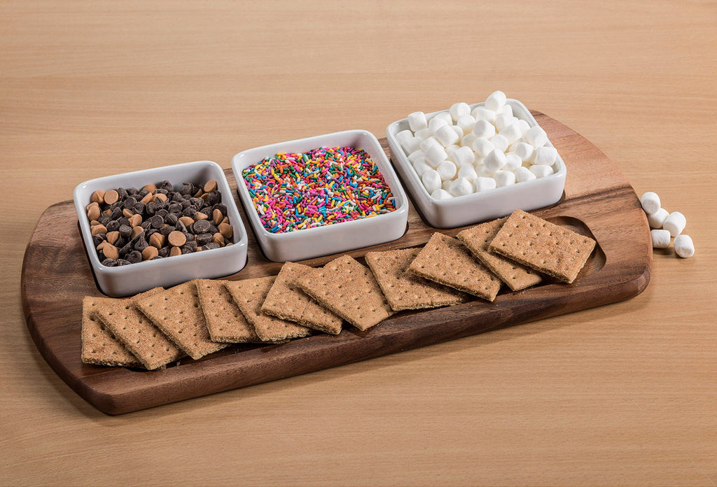 Wooden board with graham crackers, marshmallows, chocolate chips, and sprinkles on a wooden surface.
