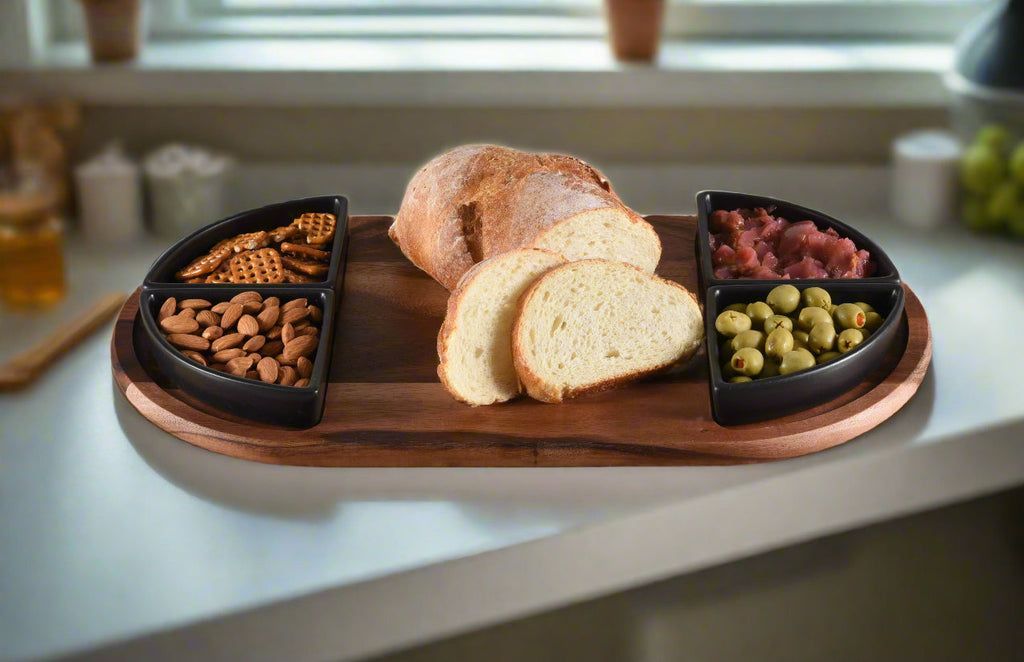 Wooden charcuterie board with sliced bread, nuts, and meats on a kitchen counter.