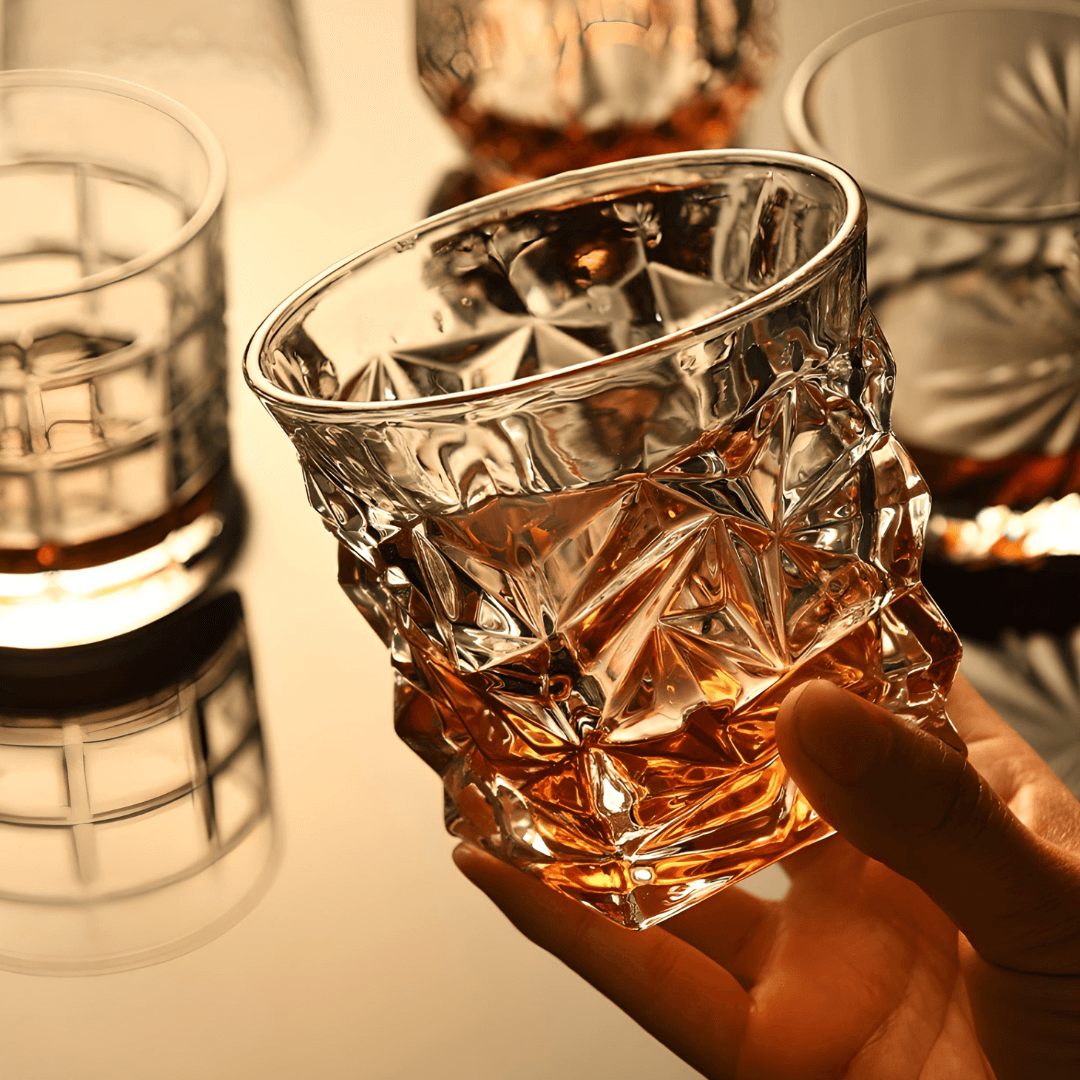 Hand holding a crystal glass with ice and whiskey, blurred background