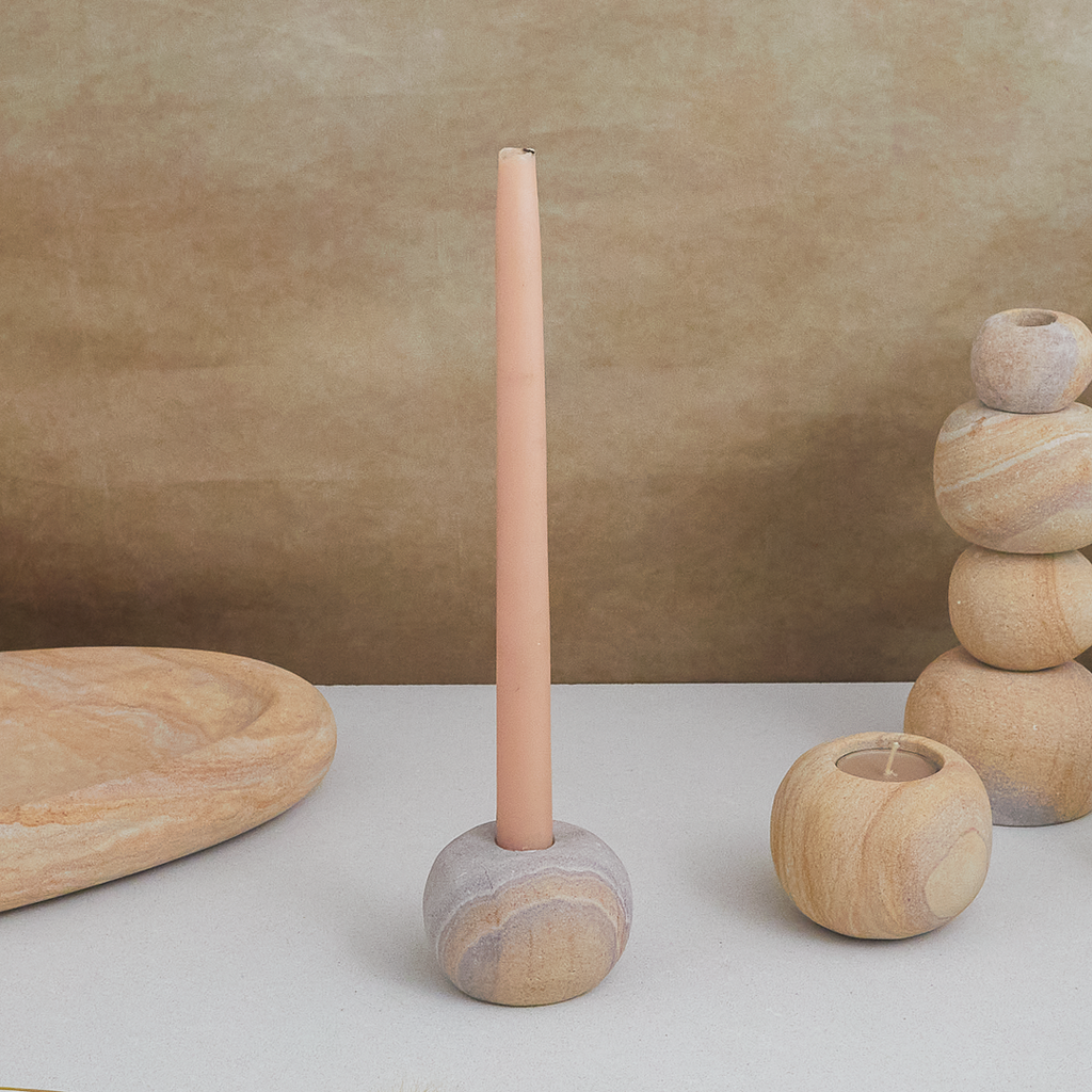 Decorative stone candle holder with a tall cylindrical candle against a beige background