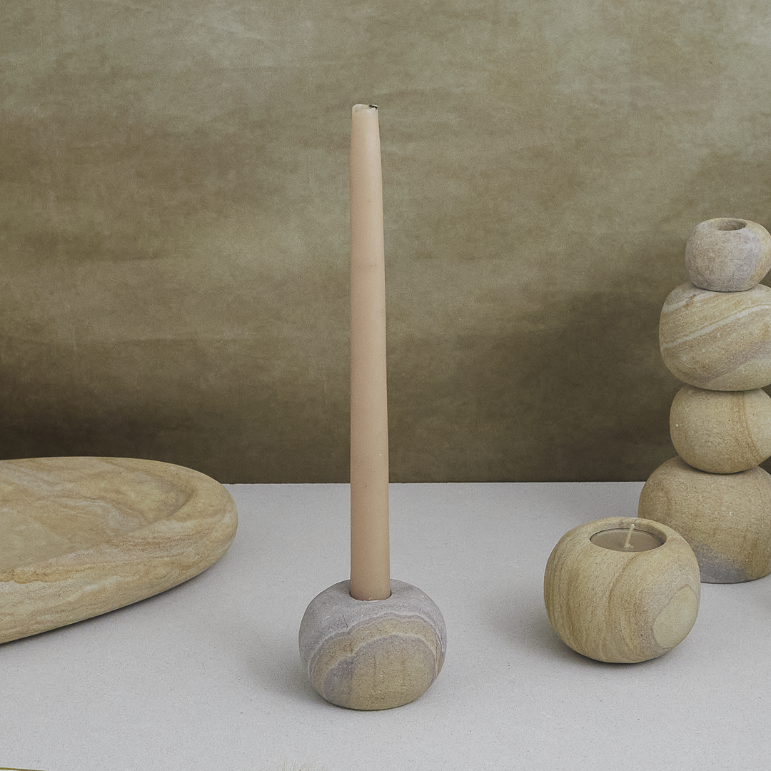 Decorative stone candle holder with a tall cylindrical candle against a beige background