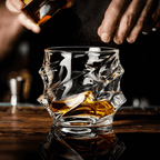 Person pouring whiskey into a textured glass on a wooden surface