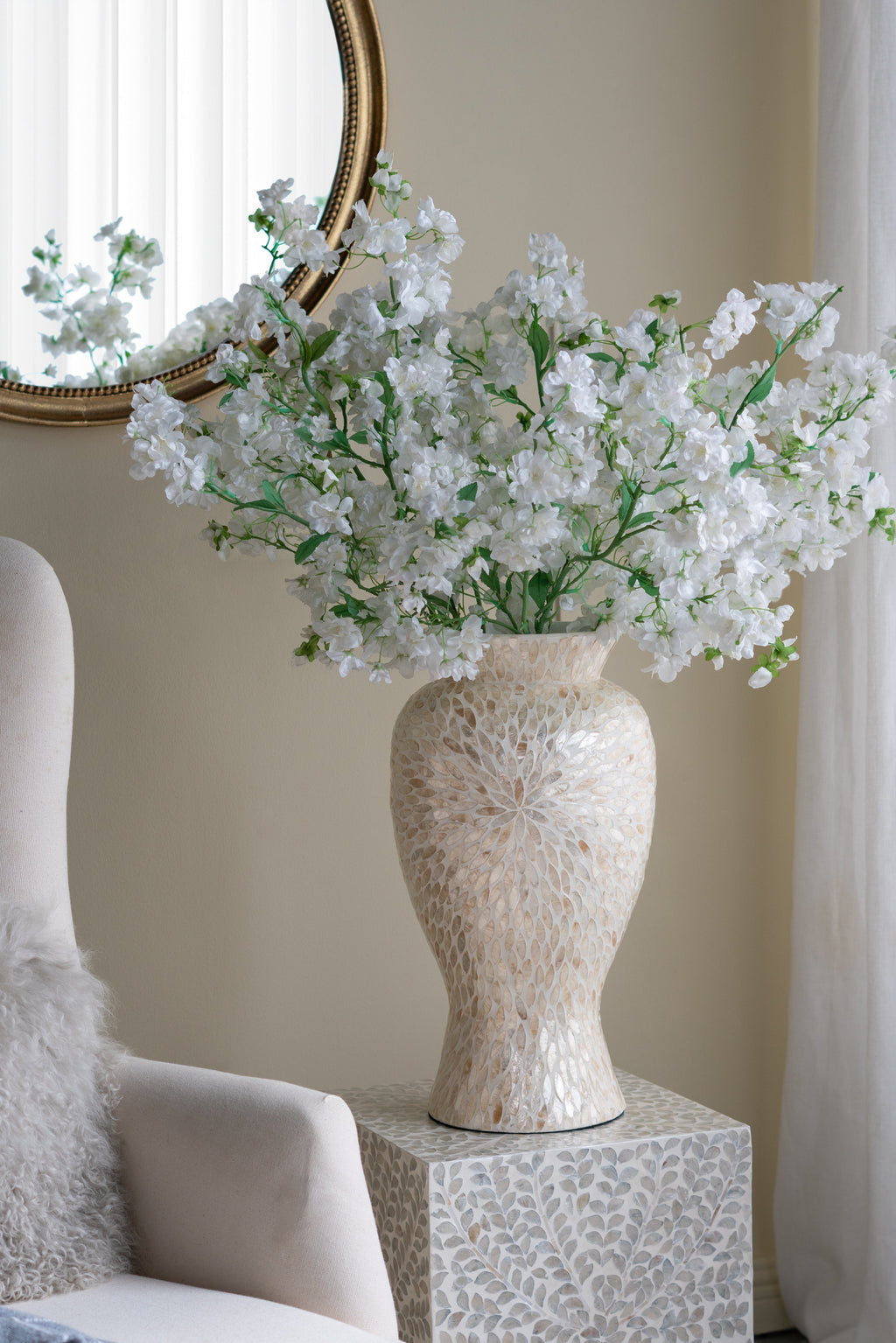 Decorative vase with white flowers on a patterned side table against a neutral wall.