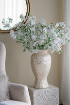 Decorative vase with white flowers on a patterned side table against a neutral wall.