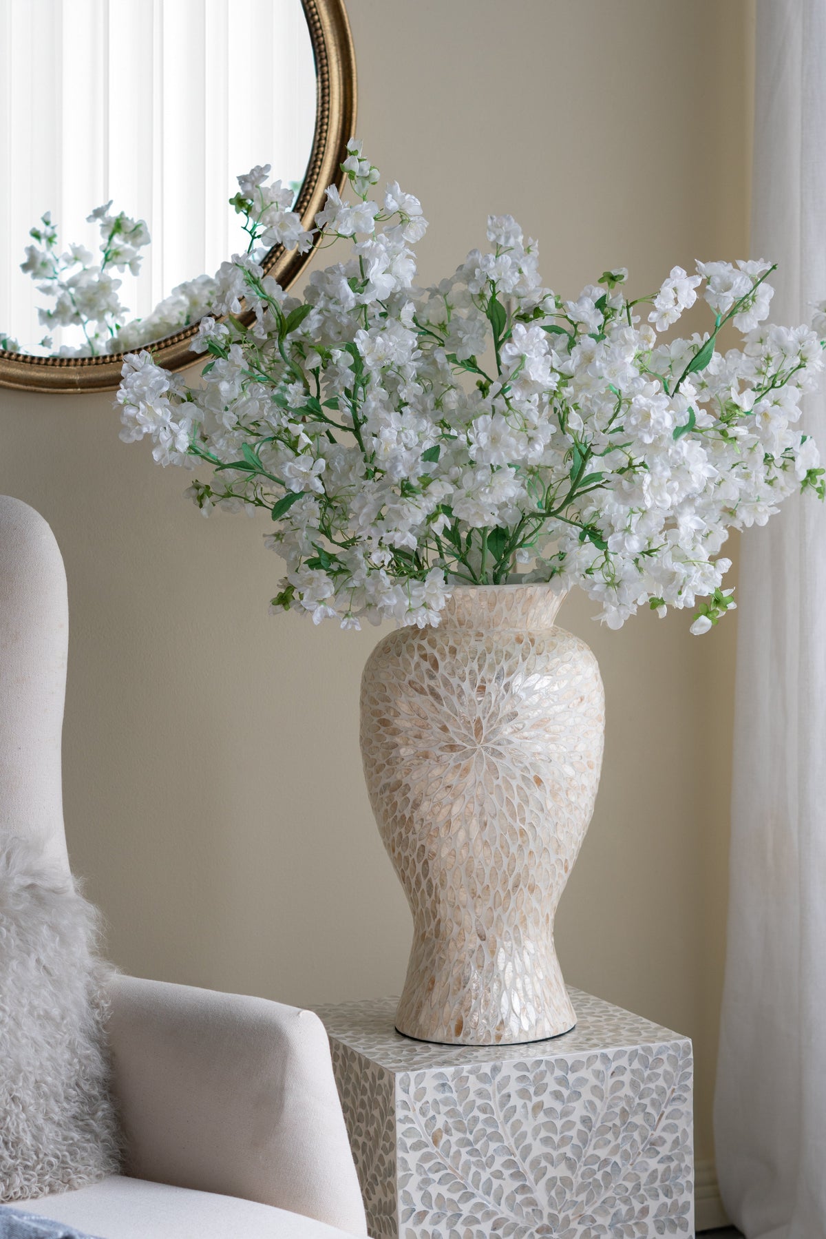 Decorative vase with white flowers on a patterned side table against a neutral wall.