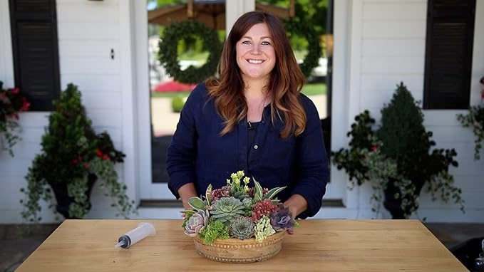 Woman standing behind a table with a decorative plant arrangement in front of a house.