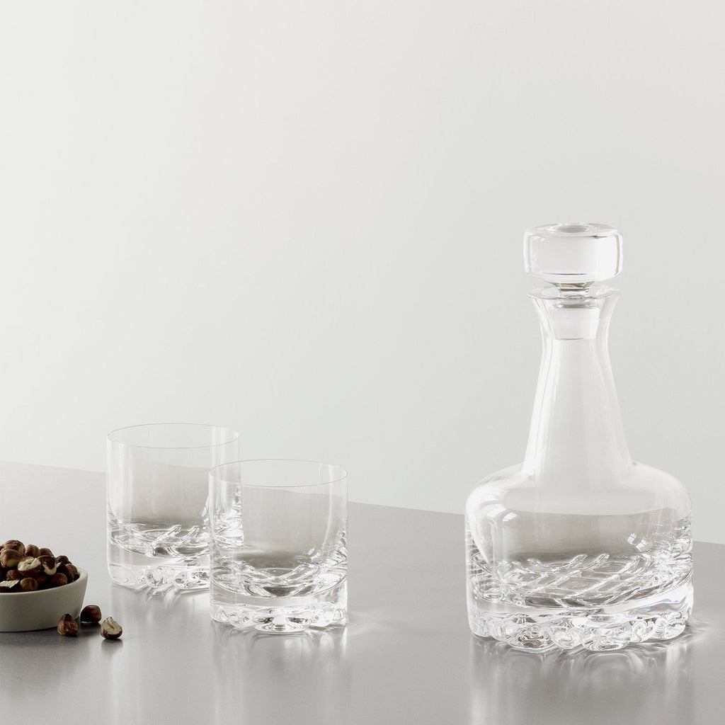 Clear glass decanter and two glasses on a light gray surface with a white background