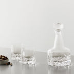 Clear glass decanter and two glasses on a light gray surface with a white background