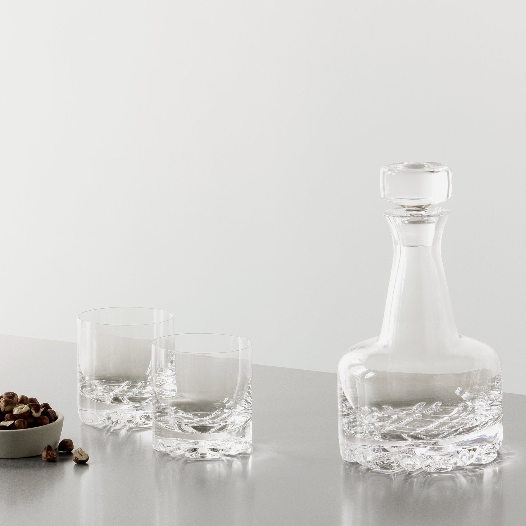 Clear glass decanter and two glasses on a light gray surface with a white background