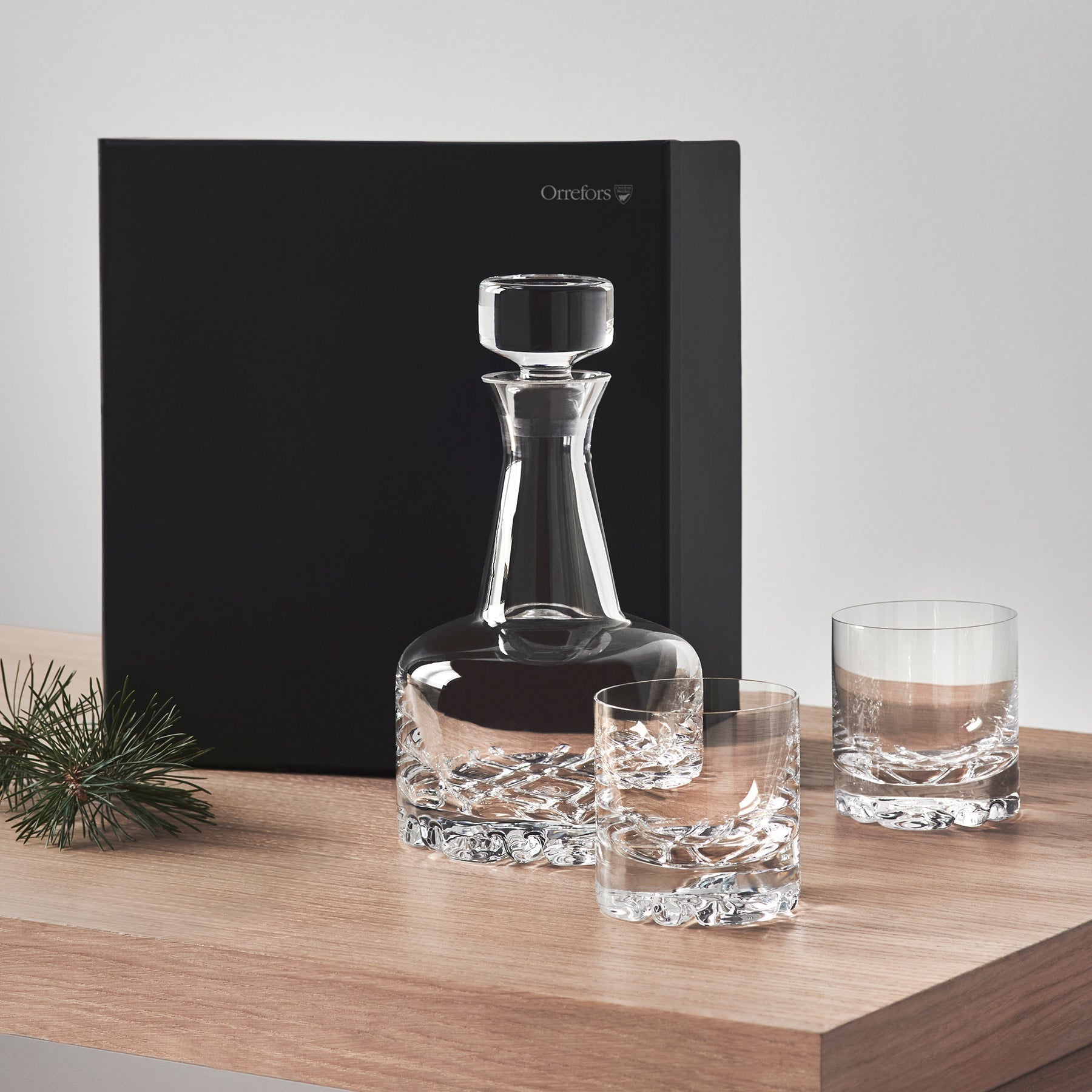 Crystal decanter and glasses on a wooden surface with a black gift box in the background.