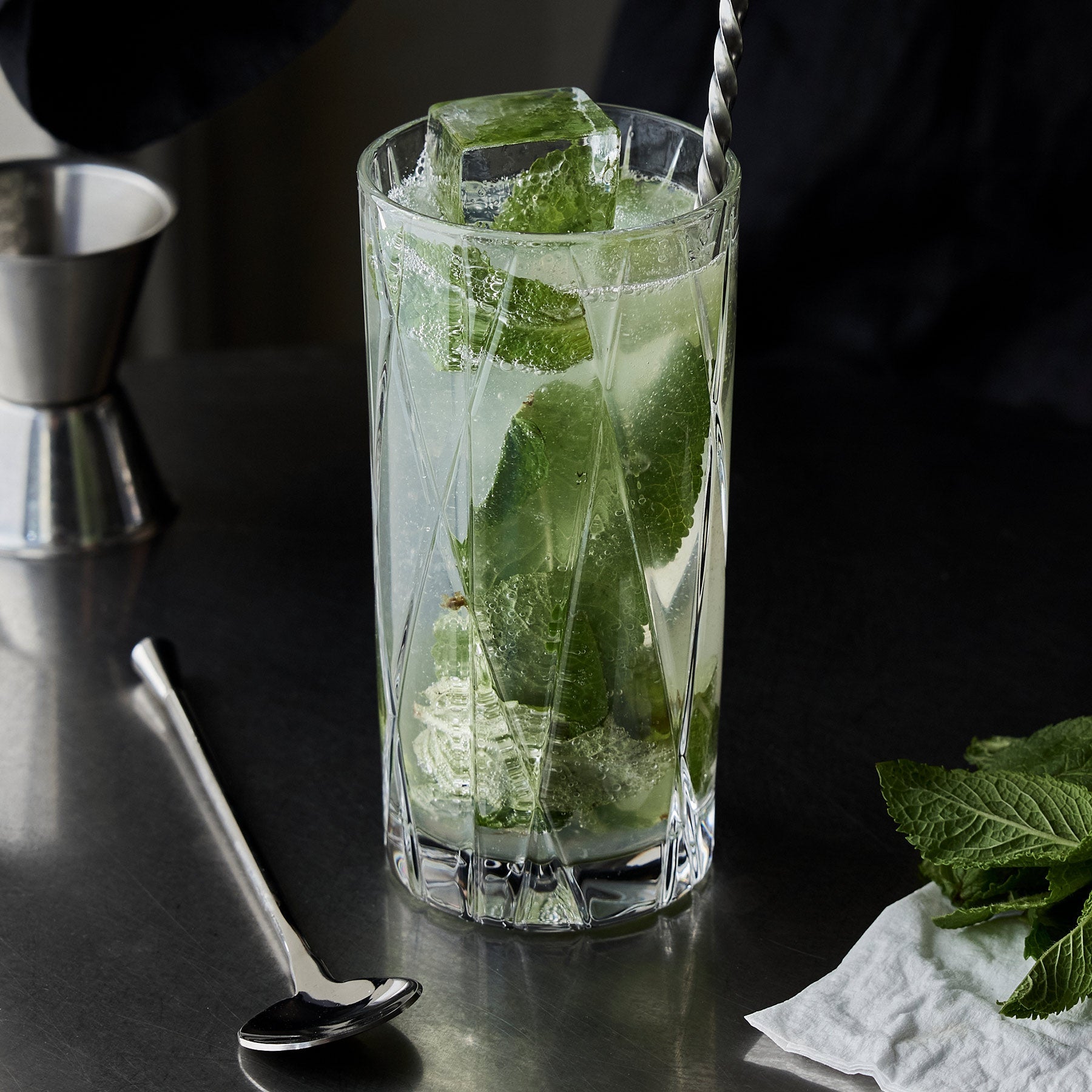 Green cocktail with ice and mint leaves in a tall glass on a dark surface.