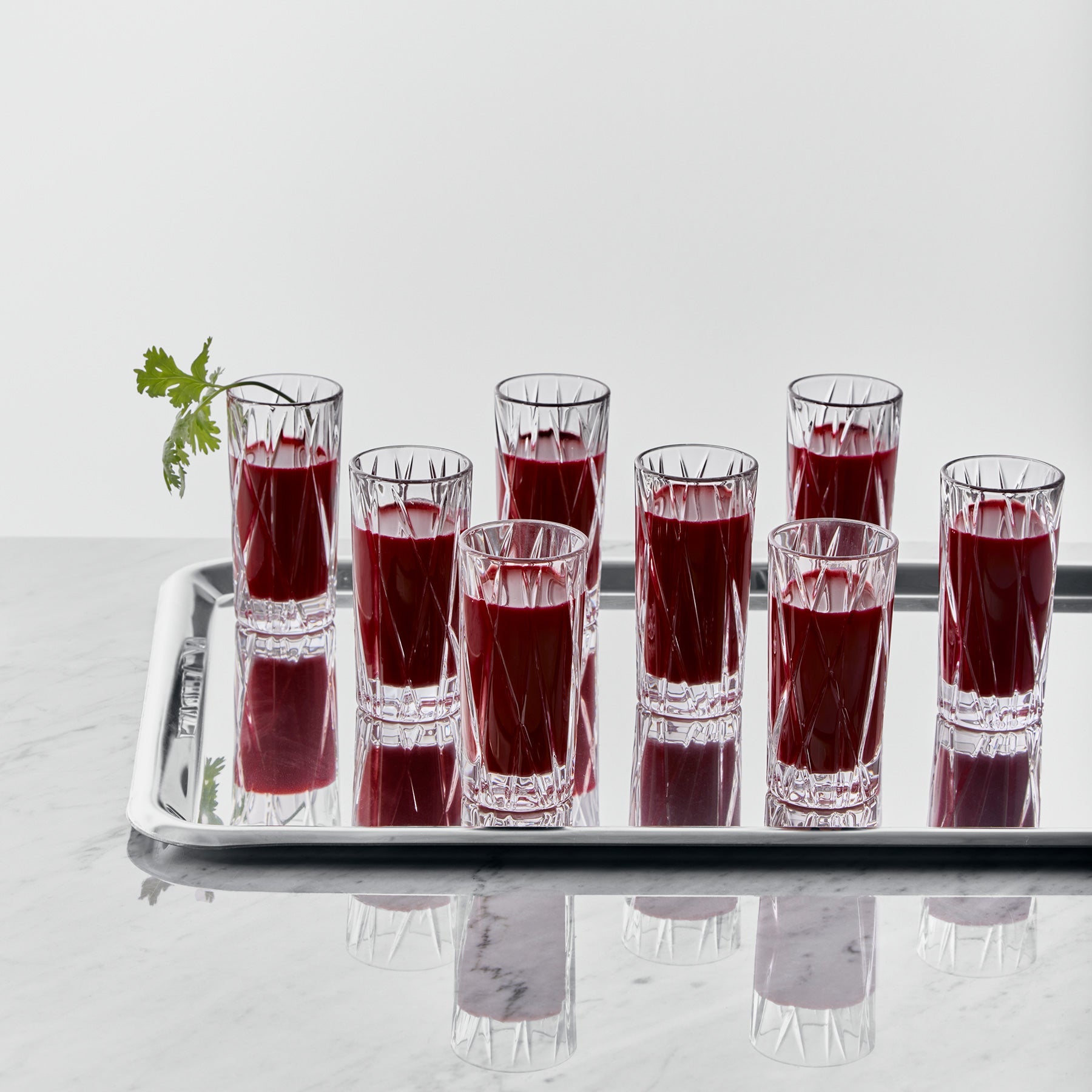 Set of clear shot glasses filled with red liquid on a white tray against a white background