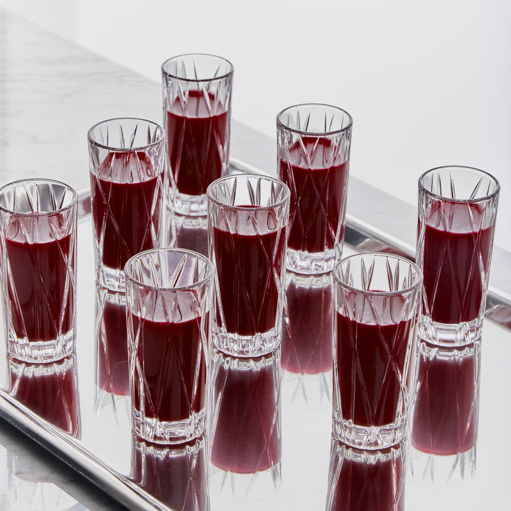 Clear shot glasses filled with red liquid on a reflective surface