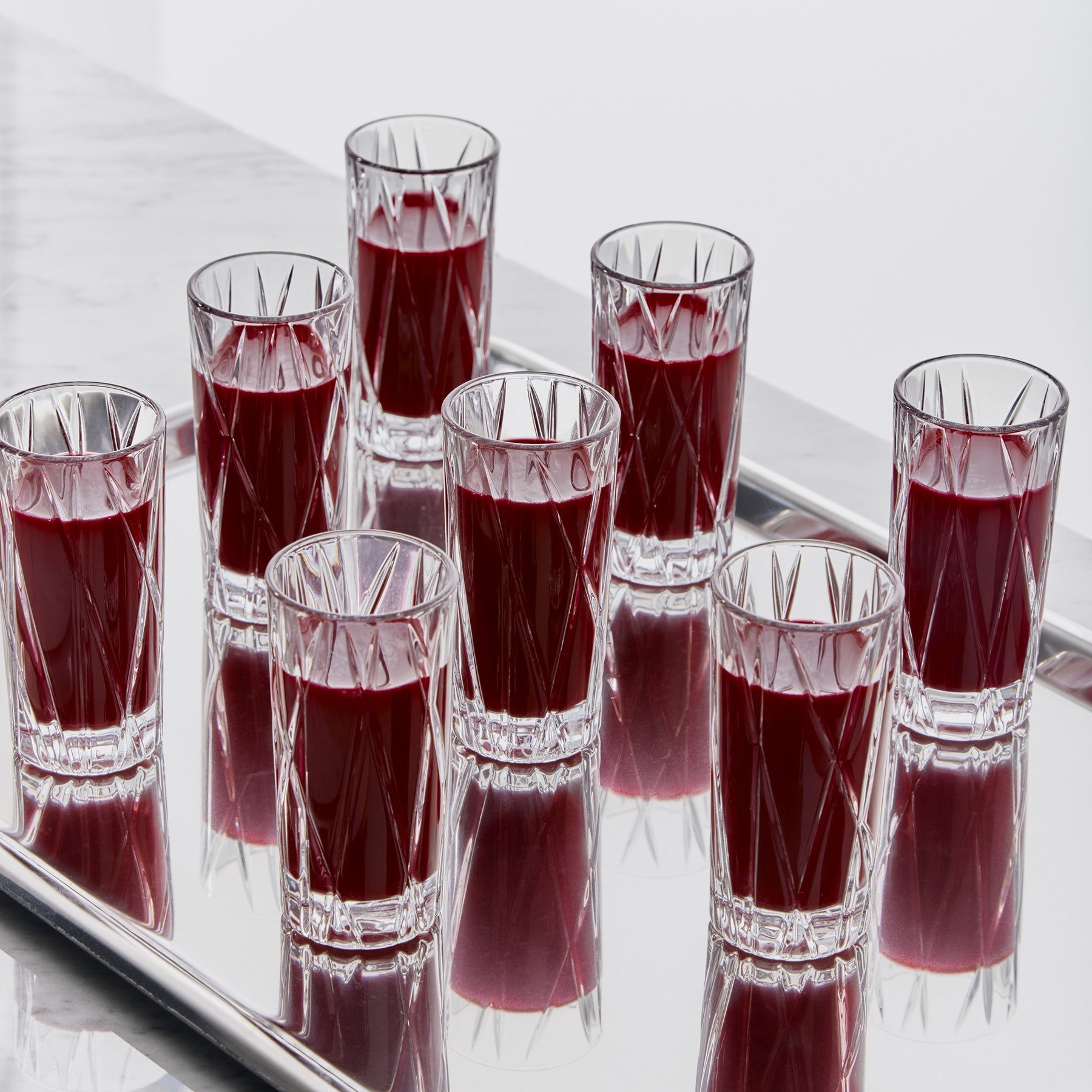 Clear shot glasses filled with red liquid on a reflective surface