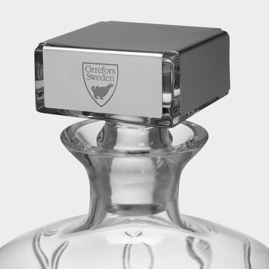 Glass decanter with a silver stopper featuring the Orrefors Sweden logo on a white background.