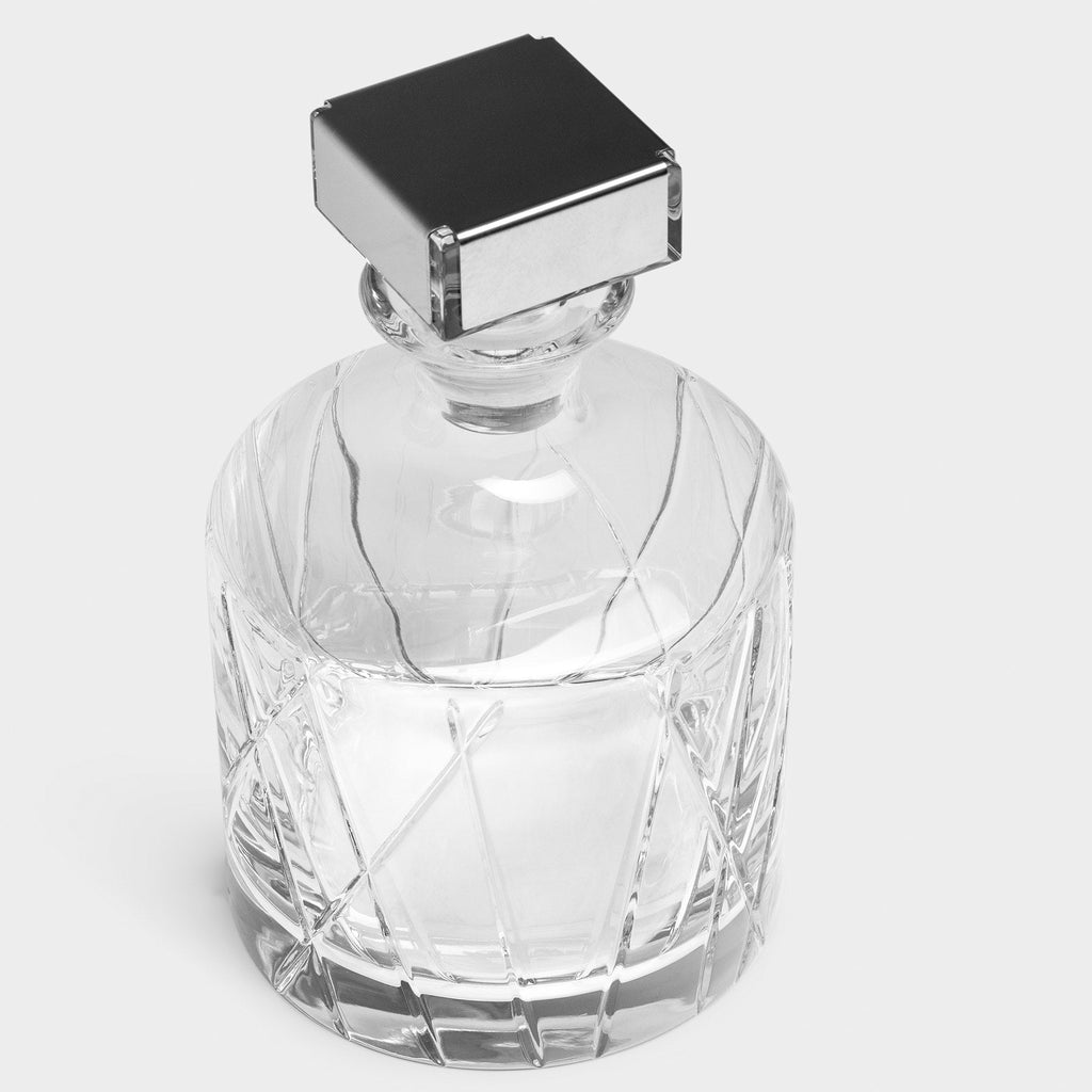 Clear glass decanter with a silver cap on a light gray background