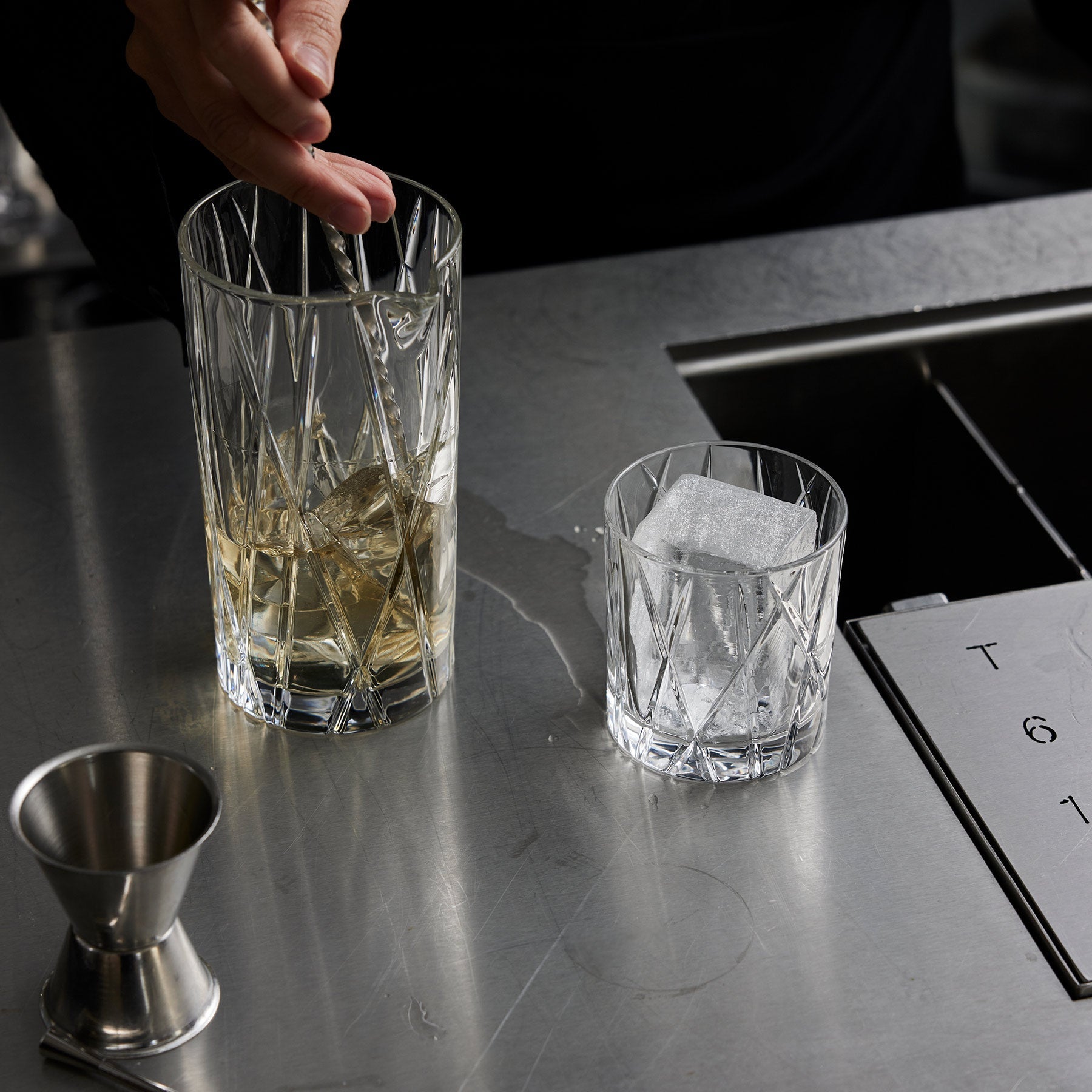 Cocktail preparation with two glasses and a jigger on a bar counter.