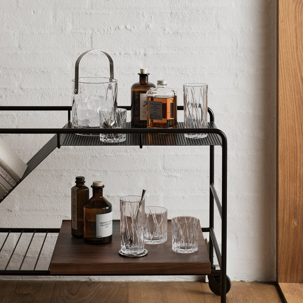 Bar cart with bottles and glasses against a white brick wall.