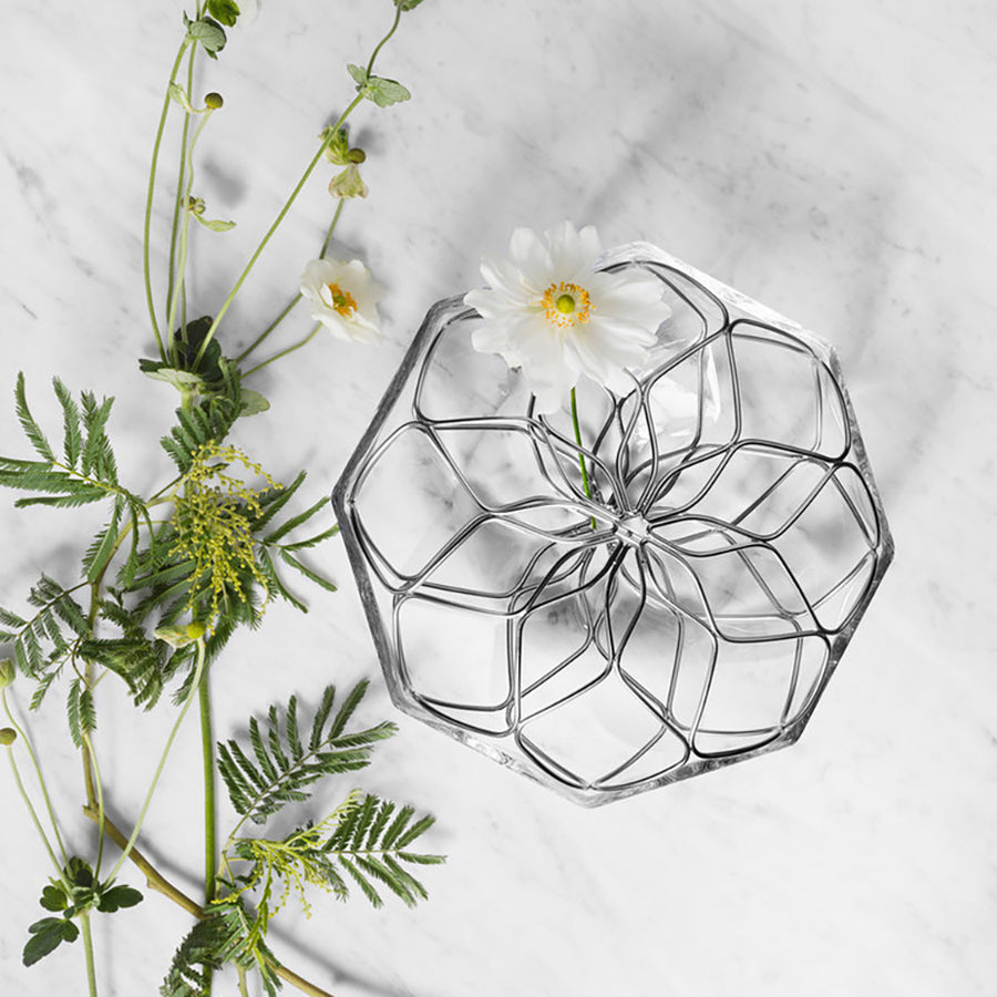 Decorative glass bowl with geometric design on a light gray surface with greenery and flowers.