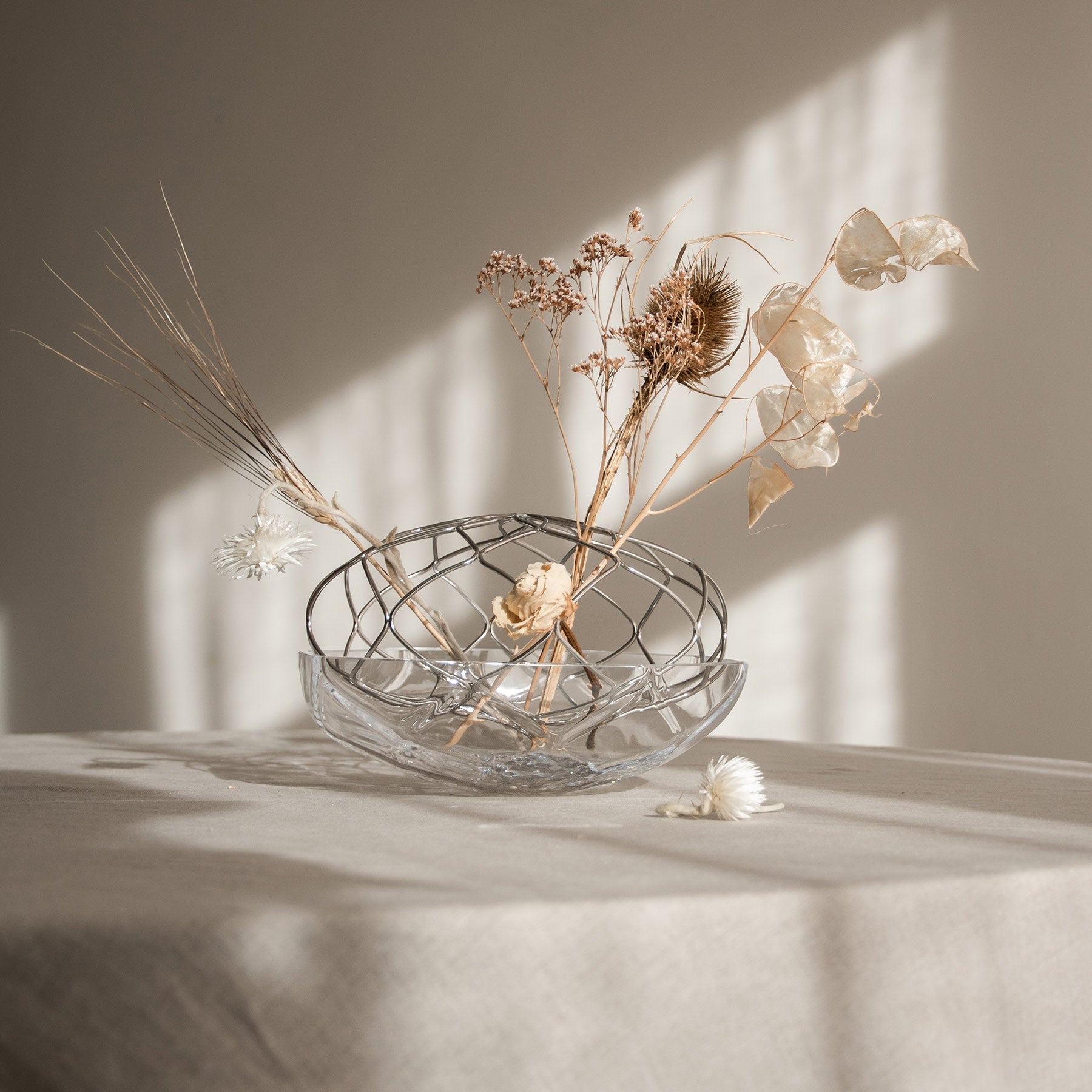 Clear glass bowl with dried flowers on a light surface with soft shadows