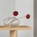 Clear glass vase with red flowers on a wooden table against a plain background