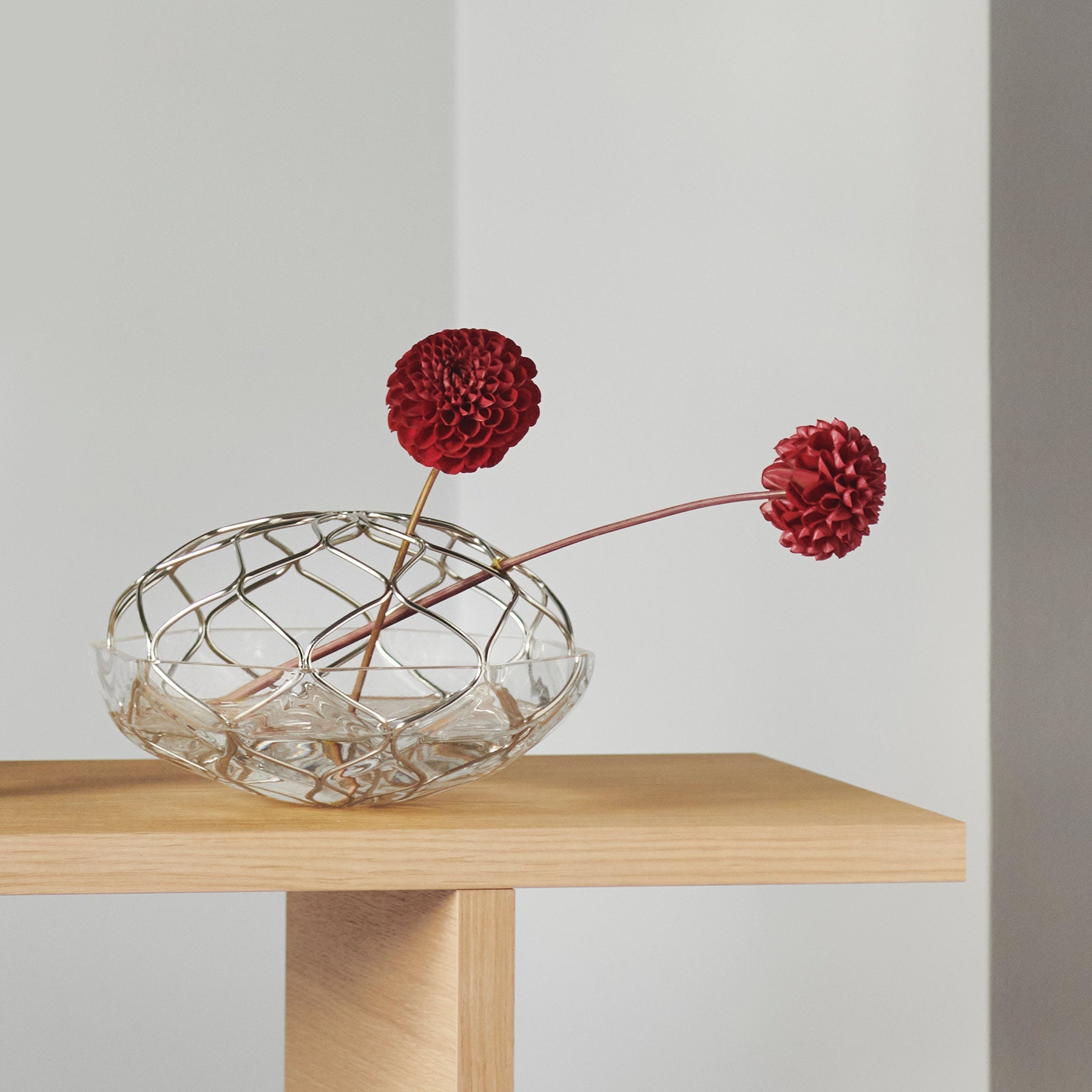 Clear glass vase with red flowers on a wooden table against a plain background