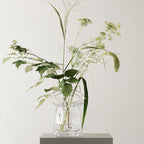 Clear glass vase with greenery against a light background
