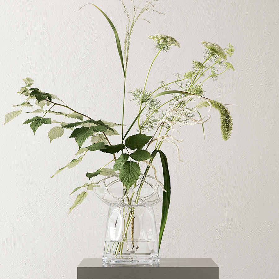 Clear glass vase with greenery against a light background