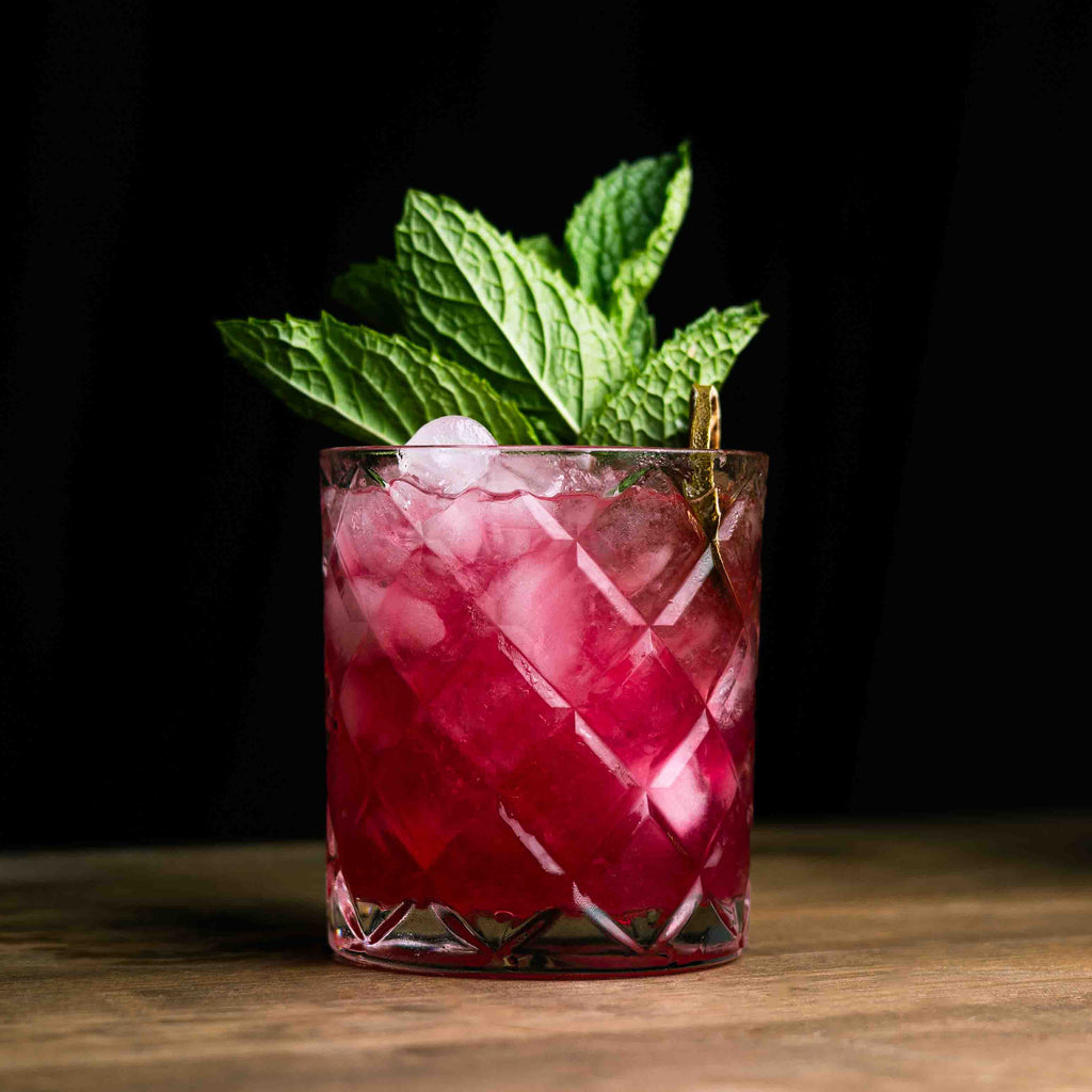 Pink cocktail with ice and mint leaves in a glass on a wooden surface.