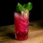 Red cocktail with lime and mint in a textured glass on a wooden surface