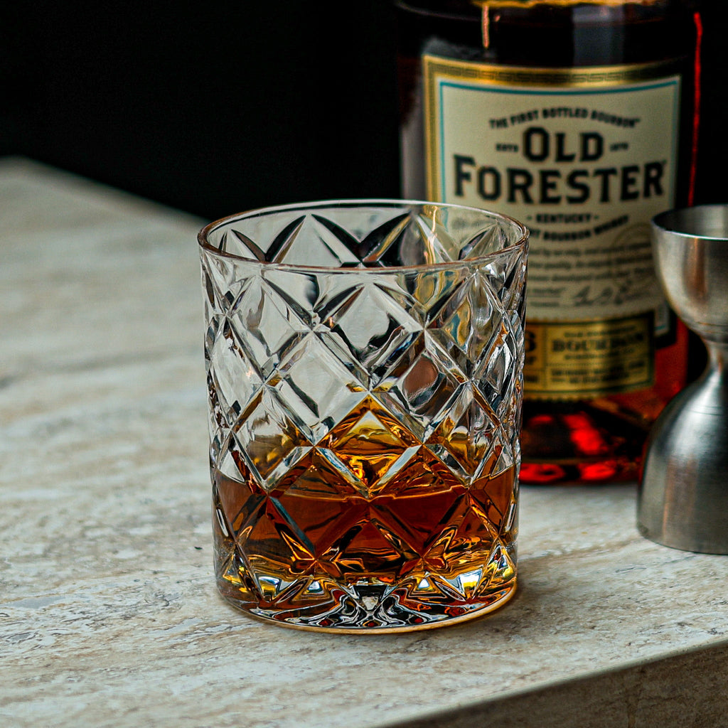 Glass of Old Forester bourbon on a wooden surface with a bottle in the background