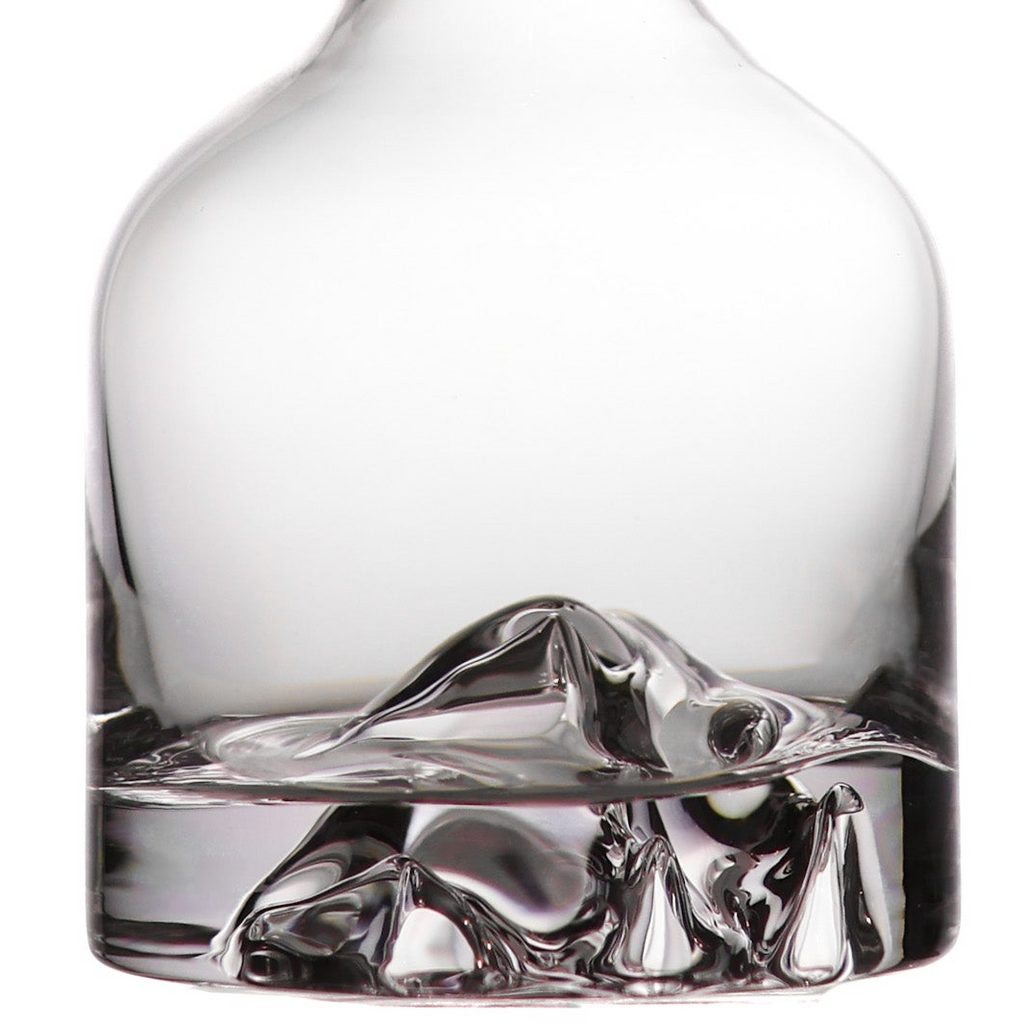 Clear glass decanter with a sculptural mountain-like base, shown close up on a white background.