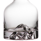 Clear glass decanter with a sculptural mountain-like base, shown close up on a white background.