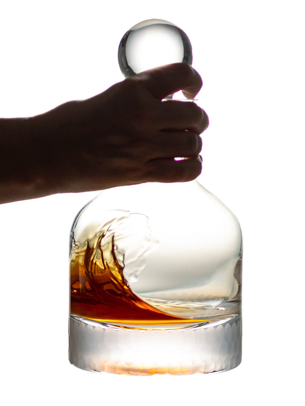 Hand holding a glass decanter with liquid against a white background