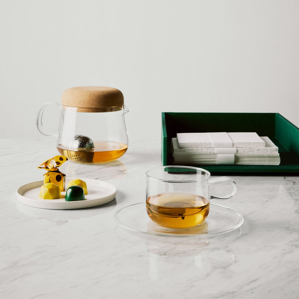 Tea set with glass teapot, cup, and tea leaves on a marble surface.