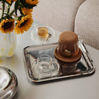 Tea set with a glass teapot and cup on a tray, sunflowers in the background