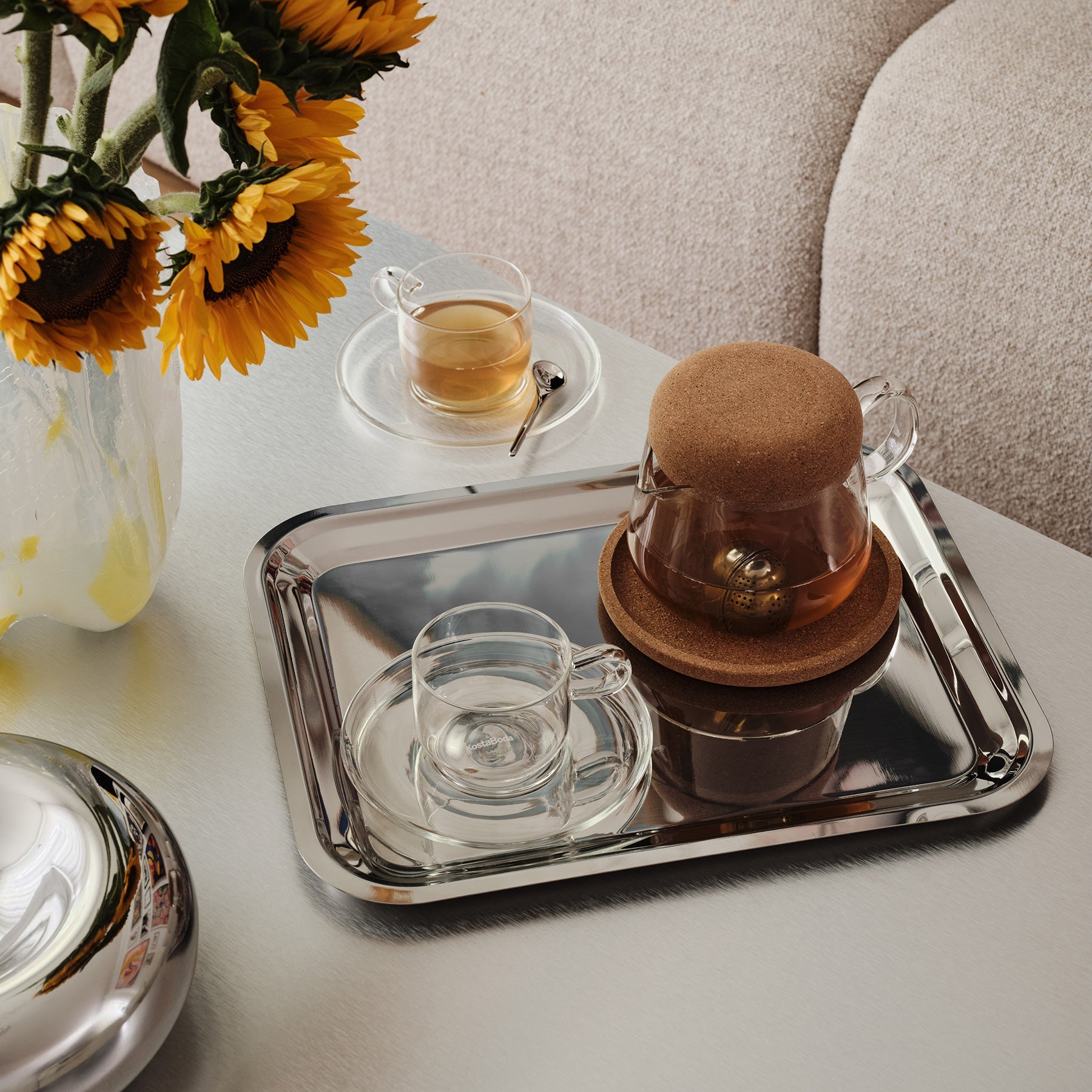 Tea set with a glass teapot and cup on a tray, sunflowers in the background