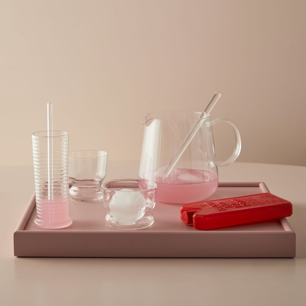 Pink glassware and accessories on a tray with a neutral background