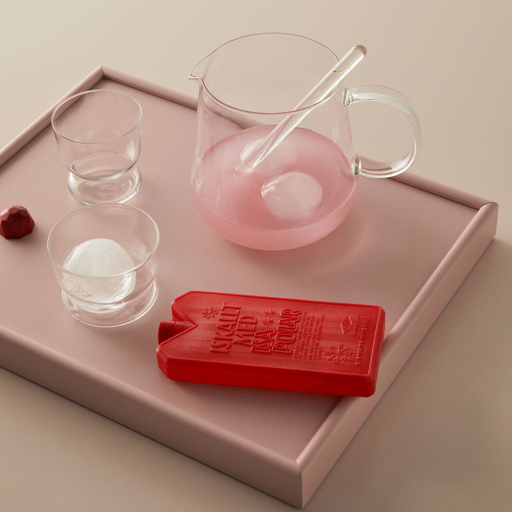 Clear pitcher with pink liquid and ice cubes on a pink tray with red mold.