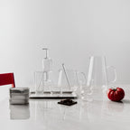 Clear glassware and kitchen items on a white surface with a red tomato.