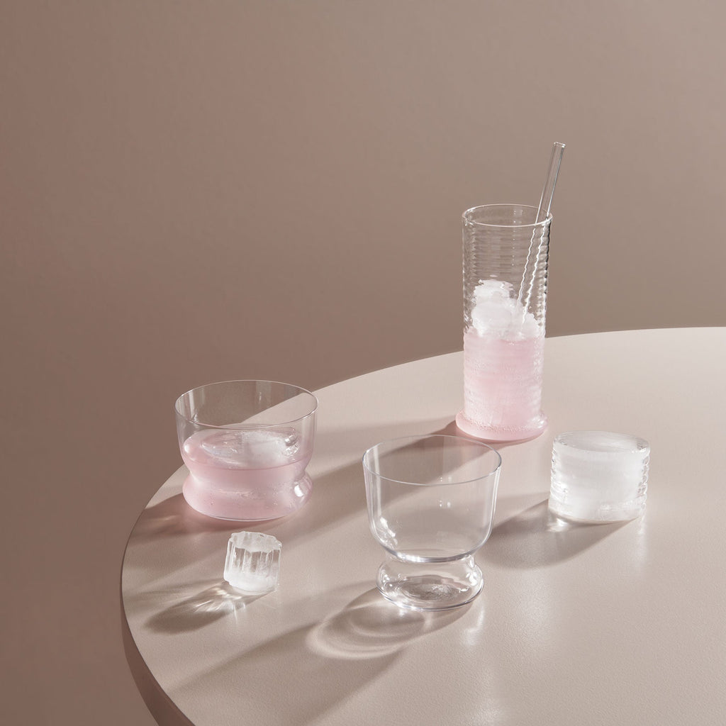 Clear glassware with pink liquid on a round surface against a beige background