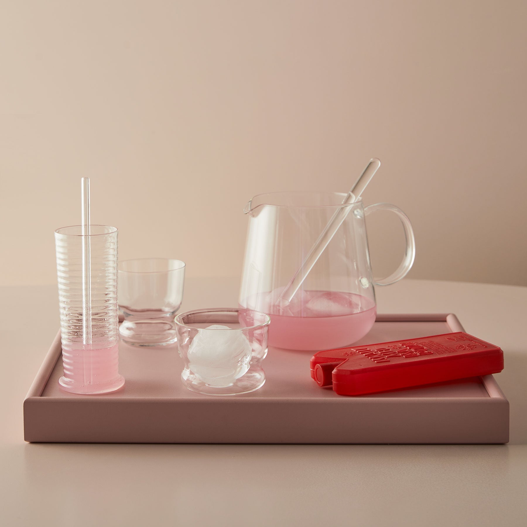 Pink glassware and accessories on a tray with a neutral background