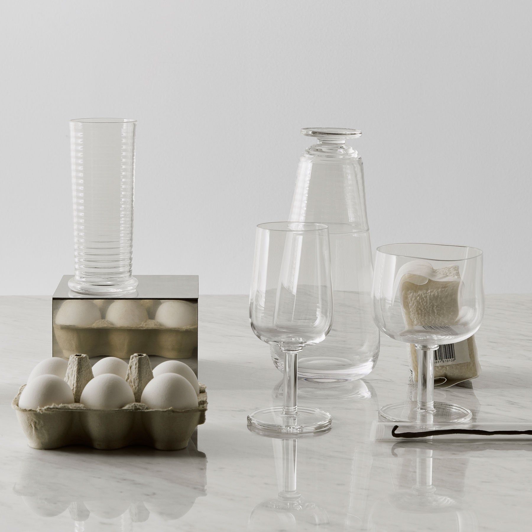 Clear glassware including wine glasses and a cup on a light surface with a neutral background