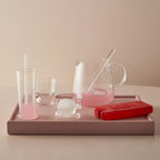 Pink glassware and accessories on a tray with a neutral background