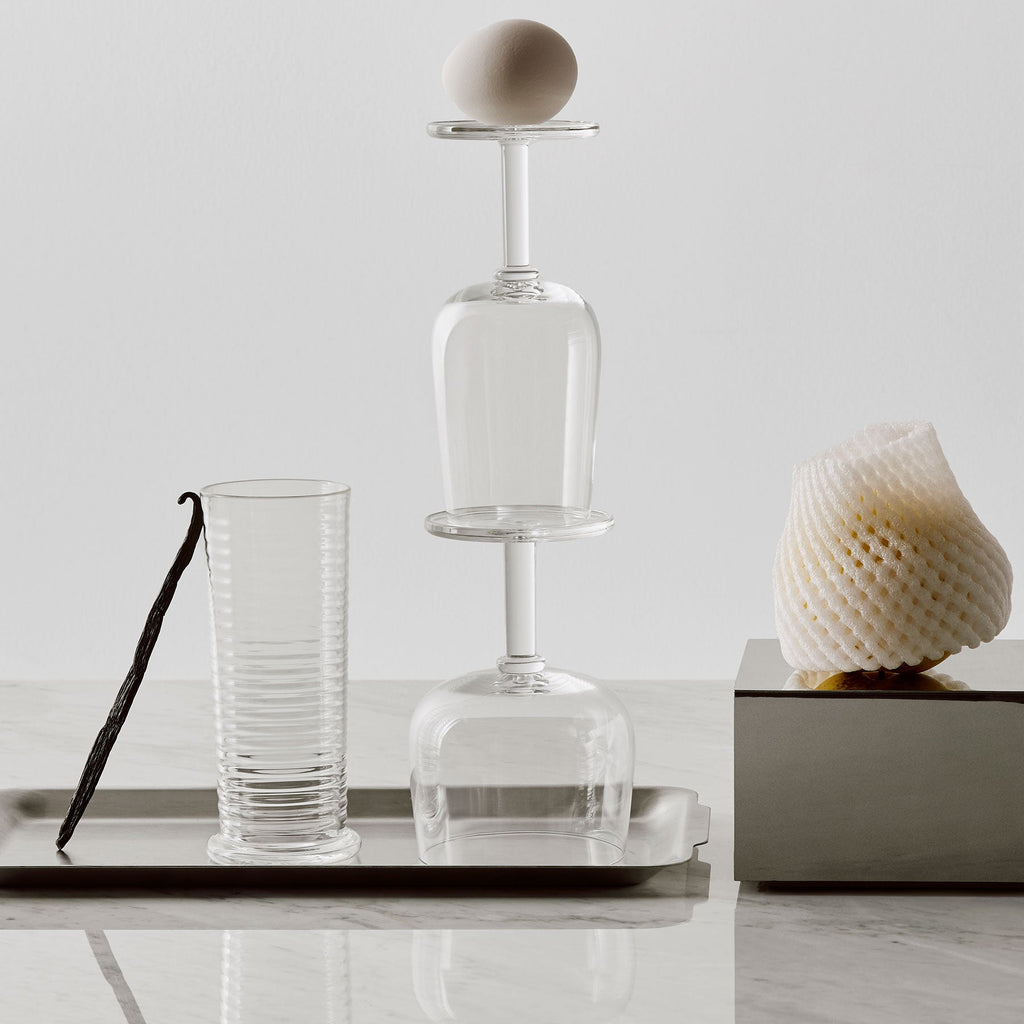 Clear glass carafe, glass tumbler, vanilla bean, and decorative shell on a white surface.