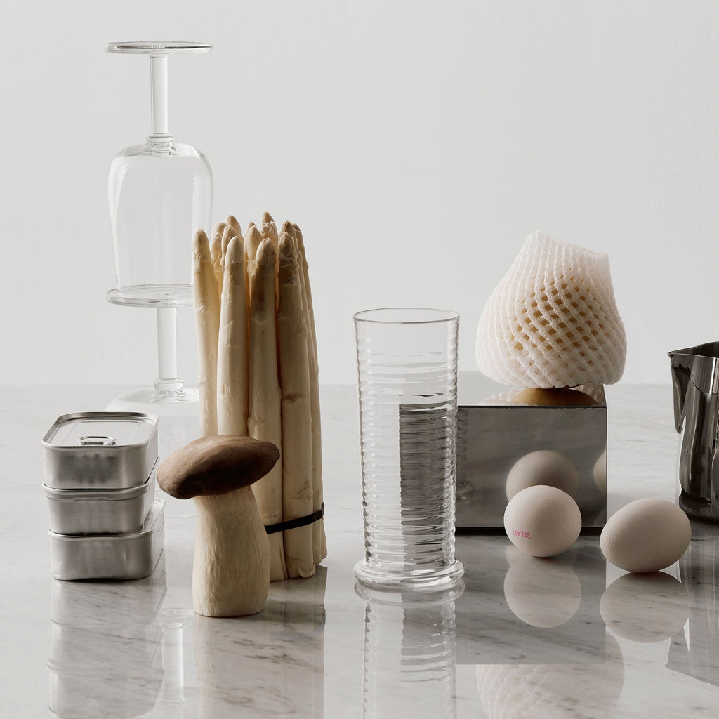 Decorative objects including a glass bottle, wooden sticks, and ceramic items on a reflective surface.